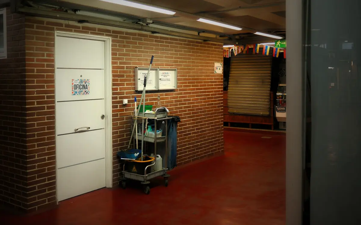 A janitorial cart with mop, bucket and supplies parked in a lit service corridor beside an office door
