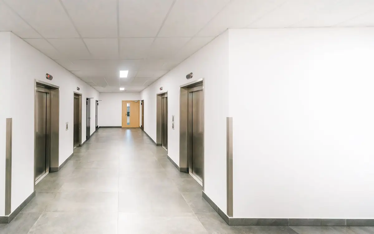 A clean office building corridor with a bank of stainless steel elevators